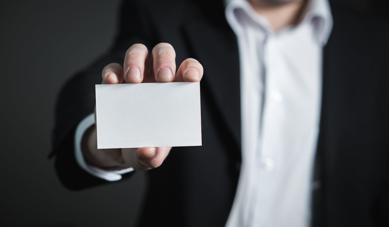 why-choose-us A man in a suit presenting a blank business card for corporate usage.