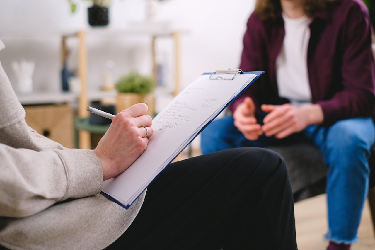 brand-03 Close-up of a therapist writing notes on a clipboard while conversing with a patient.