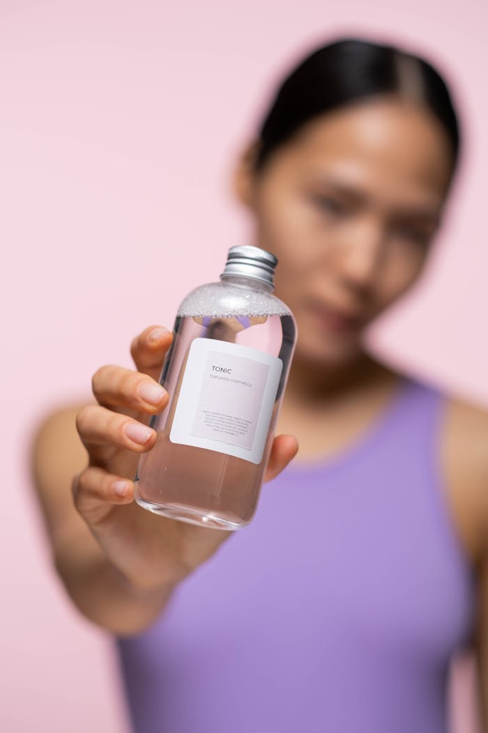 Services-02 A woman presents a skincare tonic in a studio setting with blurred background.